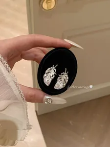 Silver feather stud earrings with shimmering diamonds shown in a detailed close-up