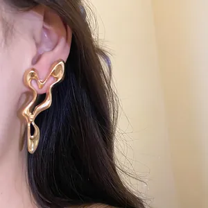 Macro shot of a model wearing large abstract gold hollow-out geometric earrings.