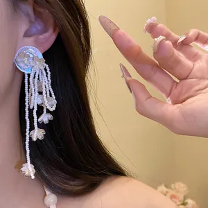 Detail of elegant white pearl flower tassel drop earrings for women on model