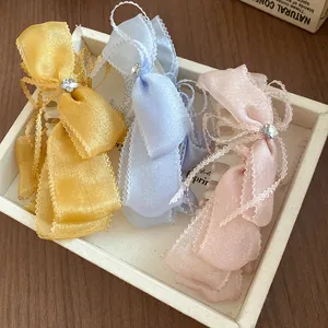 Three colorful ribbon bow hair clips with lace trim and rhinestone accents in a tray