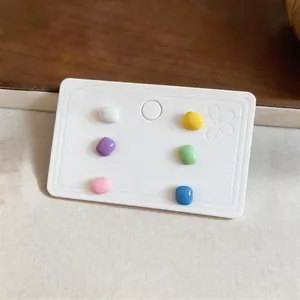 Detail view of a set of six colorful glossy square stud earrings on a white card.