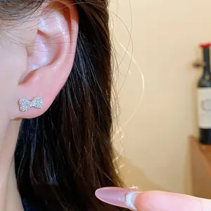 Detailed close-up showing a sparkling silver zircon bow stud earring worn on an ear