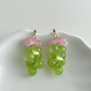 Detailed view of translucent green and pink grape cluster drop earrings on white ceramic