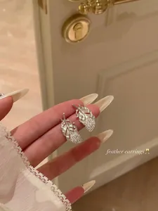 Detailed close-up showing silver feather earrings with delicate diamond pavé setting