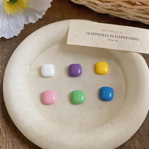 Close-up of six pairs of colorful square enamel stud earrings on a textured tray