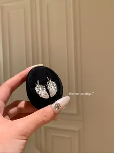 Close-up of silver-toned feather stud earrings with sparkling crystals in black box