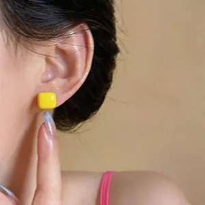 Macro view of a vibrant yellow square enamel stud earring worn by a female model