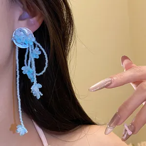 Close-up of elegant blue floral tassel earrings featuring shell details and silver needles.