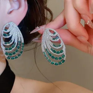 Close-up of elegant multi-layered silver earrings with green emerald-like stones and zircons.