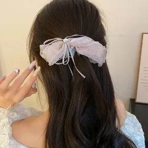 Detail view of a shimmering pink bow hair clip styled on a woman's long wavy hair.