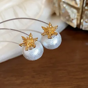 Macro detail of elegant 18k gold-plated snowflake stud earrings with white textured pearls