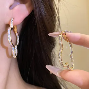 Close-up of zircon-encrusted four-leaf clover gold hoop earrings on ear and hand