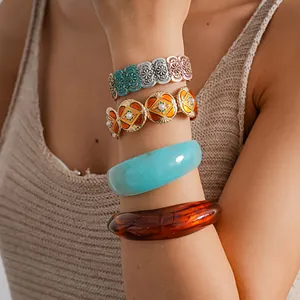 Detail view of retro metal elastic bracelets and wide resin bangles on a model's arm.