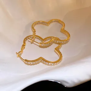 Close-up of sparkling zircon-encrusted clover hoop earrings in a golden finish.
