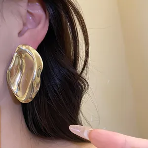 Nahaufnahme eines goldenen unregelmäßigen ovalen Metallohrrings, der am Ohr getragen wird.