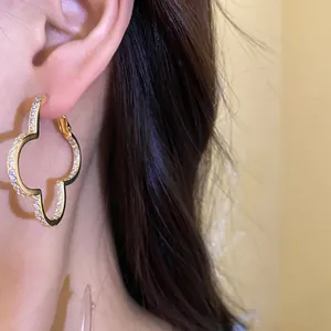 Close-up of sparkling zircon clover hoop earring on model, elegant gold-plated finish