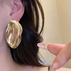 Detailansicht eines eleganten großen unregelmäßigen Gold-Metall-Ohrsteckers am Ohr