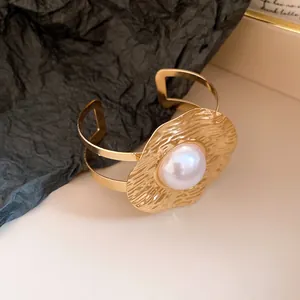 Close-up of a vintage-style gold cuff bracelet with a large pearl and textured metal plate.