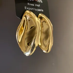 Detailansicht goldener unregelmäßiger Metall-Ohrstecker mit eleganter Wellentextur