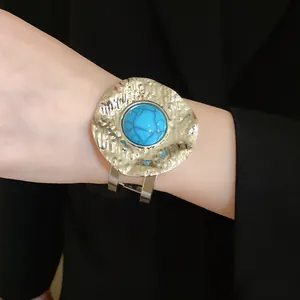 Detail shot of a vintage gold hammered cuff with a turquoise stone inlay on a wrist.