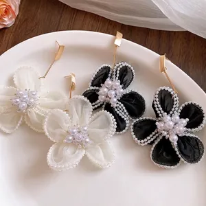 Elegant snow gauze pearl flower drop earrings in black and white on a plate.