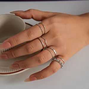 Detailed macro view of 8-piece silver geometric ring set worn on a hand holding a cup