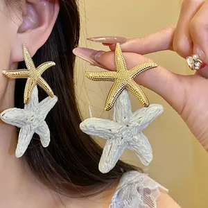 Dettaglio ravvicinato di orecchini pendenti a forma di stella marina in rafia bianca e oro