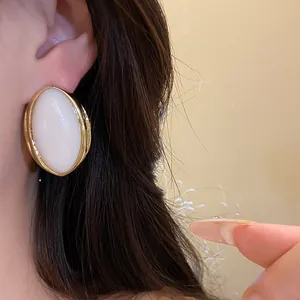 Detalle de un pendiente ovalado de resina blanca con un elegante marco de metal dorado
