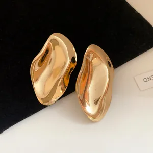 Nahaufnahme minimalistischer, unregelmäßiger Goldohrstecker aus Metall auf schwarzem Samt
