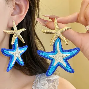 Dettaglio di orecchini a stella marina in raffia blu e bianca con piccoli perni dorati.