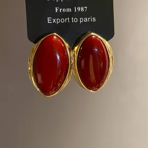 Detalle de pendientes ovalados de resina roja de estilo vintage con bordes dorados