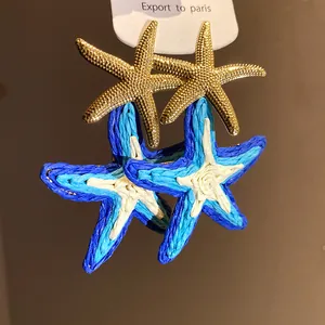 Dettaglio di orecchini a stella marina in rafia blu e bianca fatti a mano con accenti dorati