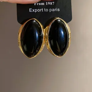Vista macro de elegantes pendientes ovalados de resina negra con borde dorado vintage