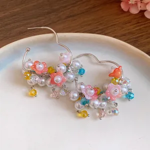 Detailed view of silver needle earrings featuring pearls and colorful resin flower pendants