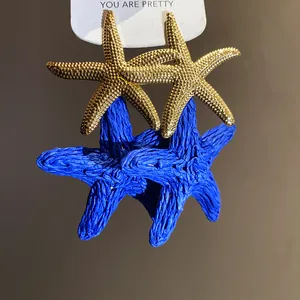 Dettaglio degli orecchini a stella marina in rafia blu e metallo dorato per le vacanze estive.