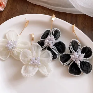 Detail view of elegant snow gauze flower earrings with pearls in black and white.