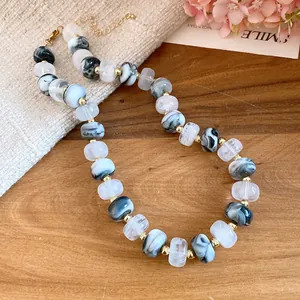 Detailed view of handmade marble pattern beaded necklace with gold spacers on wooden background.
