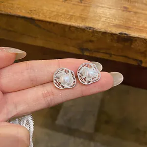 Detail view of elegant silver flower-shaped stud earrings with center pearl on hand