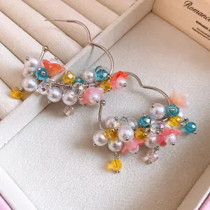 Close-up of elegant floral hoop earrings with pearls and colorful beads in a box.