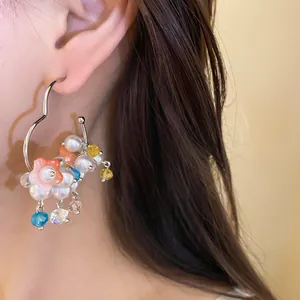 Detail macro view of a colorful pearl flower pendant hoop earring worn by a model.