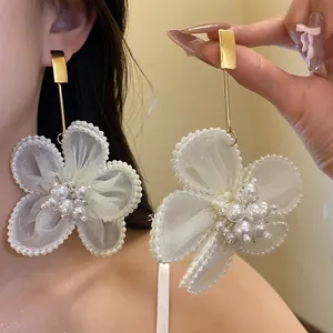 Detail view of large snow gauze pearl flower drop earrings with golden stud
