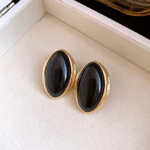 Primer plano de los pendientes de resina negra de estilo francés vintage con borde dorado