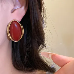 Detalle de pendientes retro ovalados de resina roja con borde dorado en la oreja.