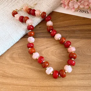 Close-up of handmade geometric beaded necklace in red, orange, and light pink tones.