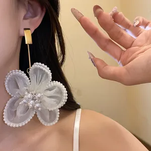 Detailed view of oversized white tulle flower earrings adorned with pearls on a model