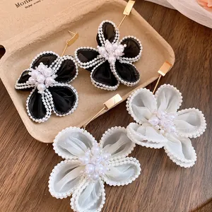 Detail view of elegant black and white snow gauze flower earrings with pearl clusters and gold posts.