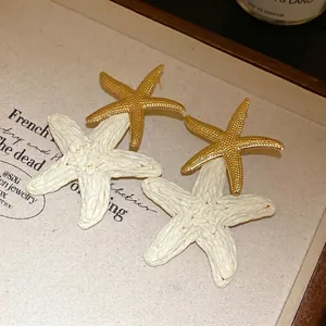 Dettaglio orecchini a stella marina in rafia con trama intrecciata e dorata