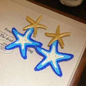 Dettaglio orecchini a stella marina in raffia blu intrecciata con dettagli dorati