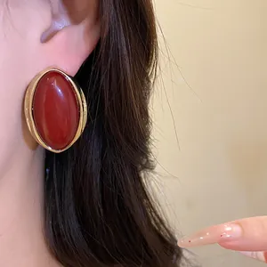 Elegantes pendientes de botón ovalados de resina roja retro con borde dorado en un modelo