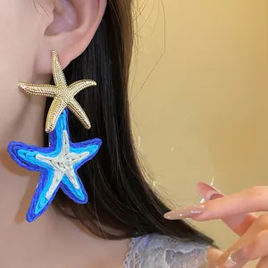 Dettaglio di orecchini a stella marina in raffia blu e oro per uno stile estivo